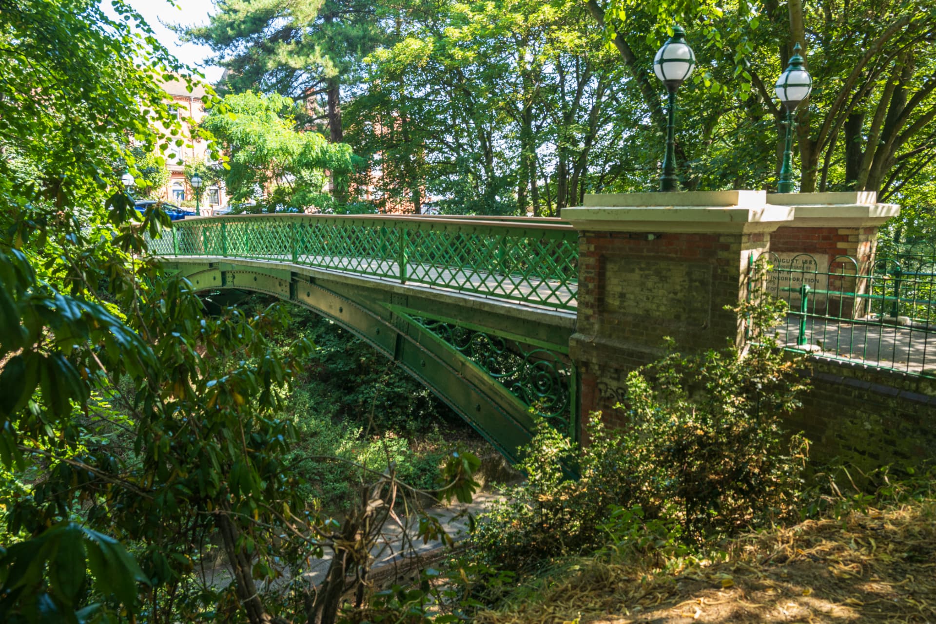 An ornate green Victorian footbridge crossing a wooded park in Lowestoft