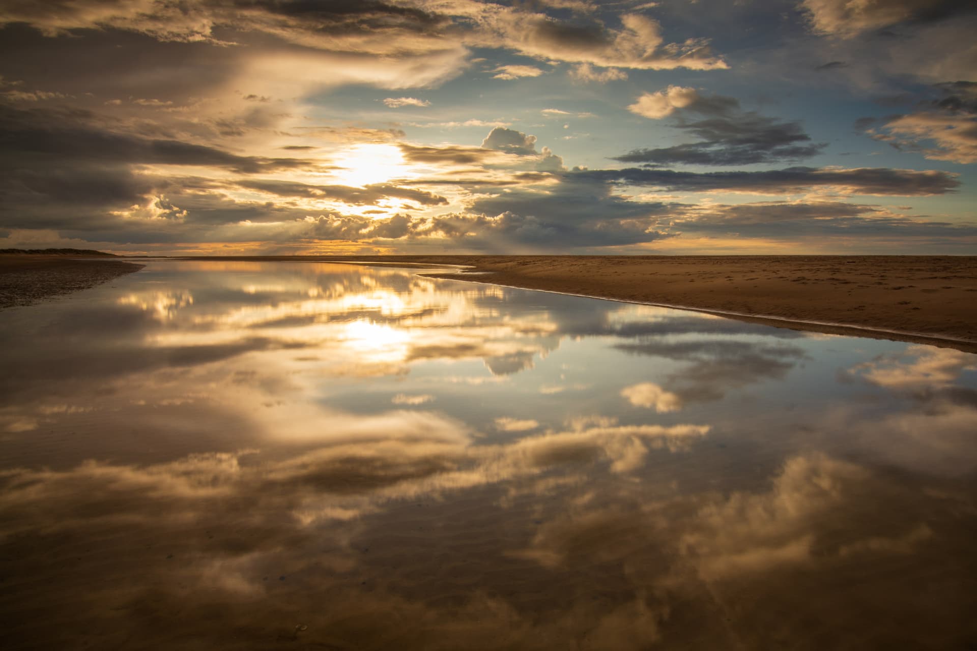 Golden sunlight breaking through clouds over calm water and smooth sand