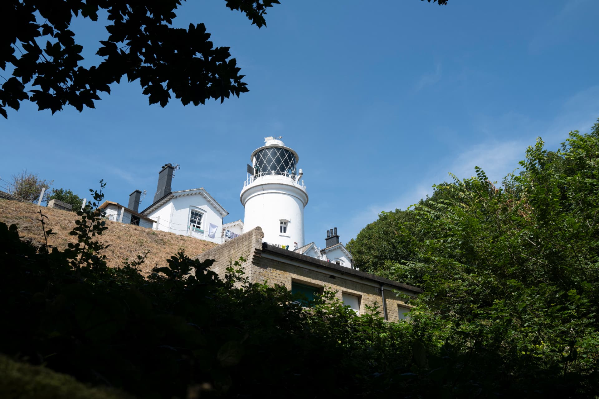 Lowestoft Lighthouse rising above greenery and cottages on a clear day